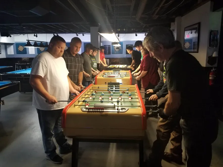 A league night in a bar's back room: players lined up along two foosball tables